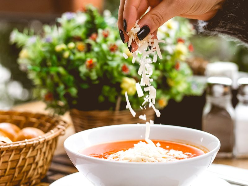 side view a woman sprinkles tomato soup grated cheese and crackers